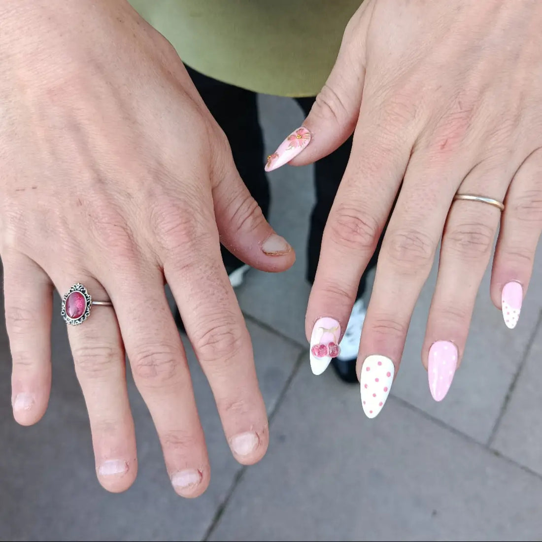 Comparaison de deux mains : l'une avec des ongles rongés courts, l'autre avec de beaux press-on nails roses en forme amande avec nail art floral et polka dots