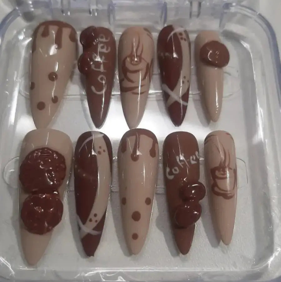 Set de 10 faux ongles Coffee Dreams dans leur boîtier transparent, présentant des designs café et chocolat avec des motifs variés en nuances de brun et beige, finition brillante professionnelle