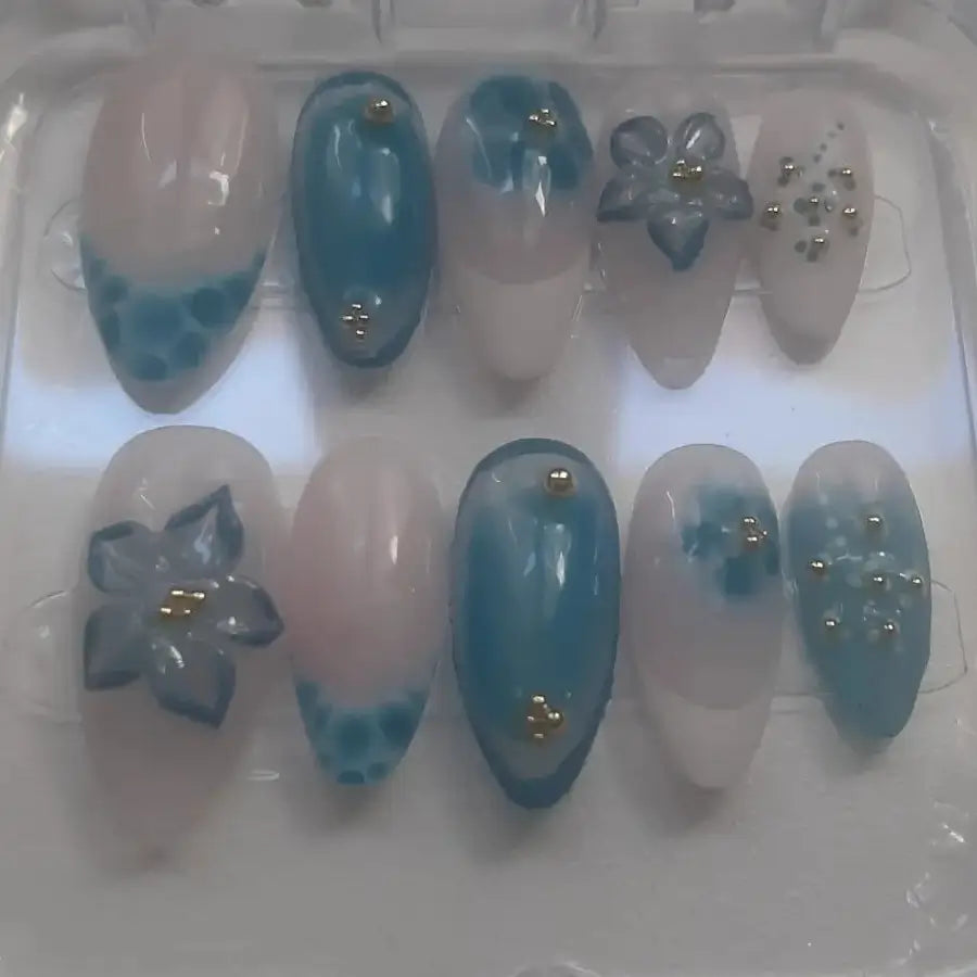 Set de 10 press-on nails , présentant des ongles avec bases transparentes et nuances bleutées, ornés de fleurs 3D translucides aux centres dorés et de strass dorés
