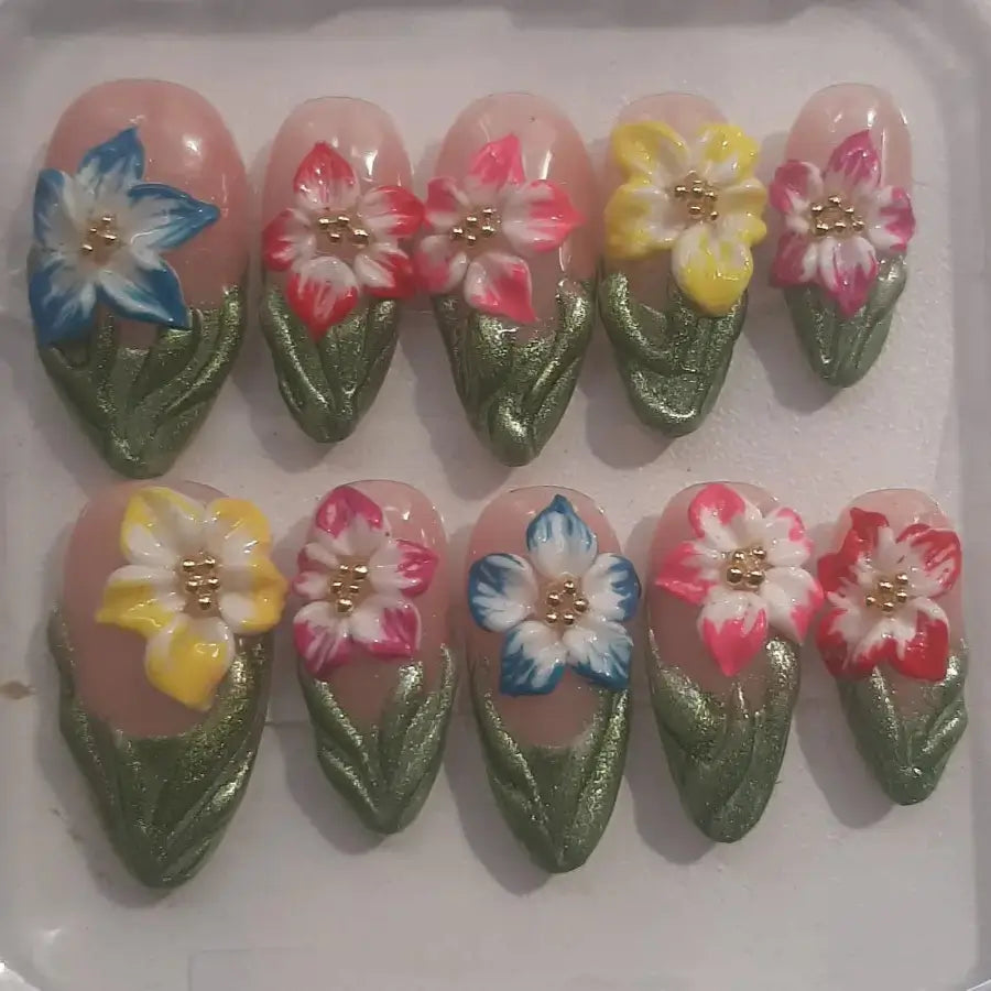 10 press-on Capucine disposés présentant des motifs floraux peints à la main en couleurs pastel (bleu, rose, jaune, blanc) avec des détails dorés et des feuillages verts métallisés