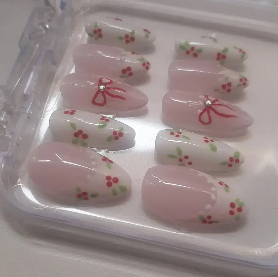 Ajoutez une touche de douceur romantique à votre look avec ces magnifiques faux ongles rose poudré ornés de délicates cerises rouges et de nœuds charmants.