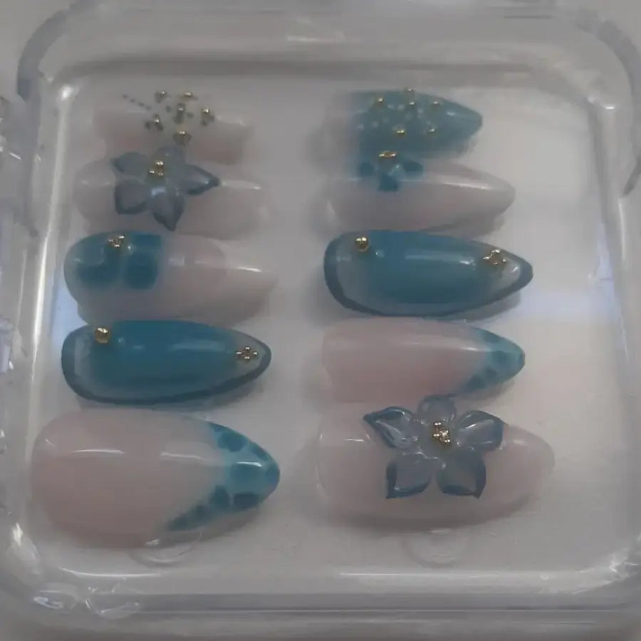 Vue sur le coôté détaillant des press-on nails présentant des ongles avec bases transparentes et nuances bleutées, ornés de fleurs 3D translucides aux centres dorés et de strass dorés