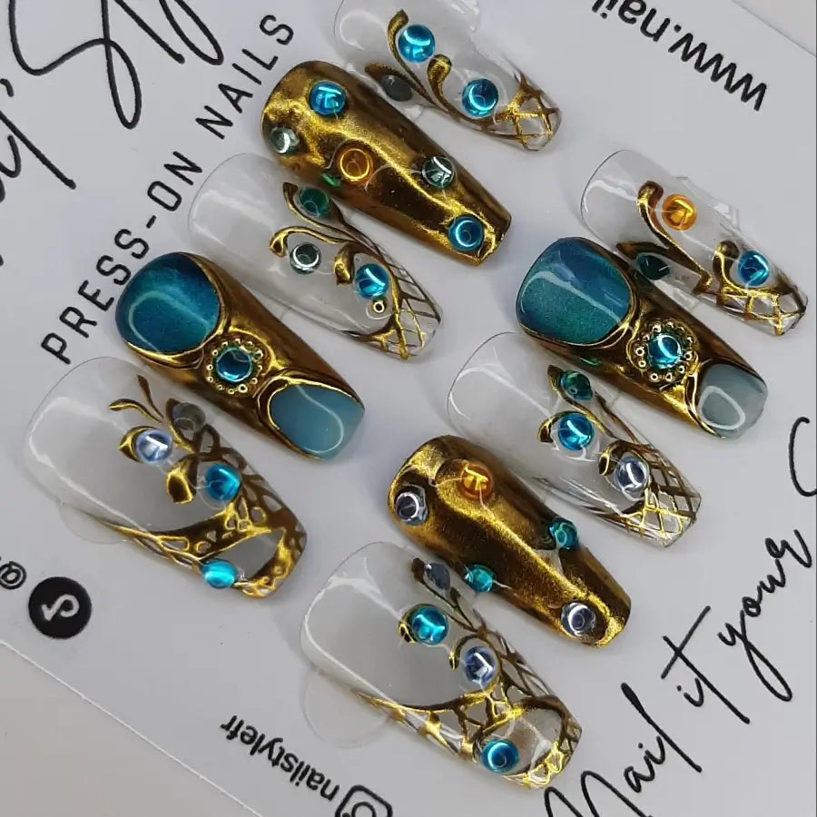 transparence, or et bleu se marient pour donner un look bijou à ces faux ongles très luxueux. Press-on nails faits main en France, fabrication artisanale française. tendance 2026. sur une base nude, bleu cat eyes et chrome doré réhaussés de strass. Forme coffin médium
