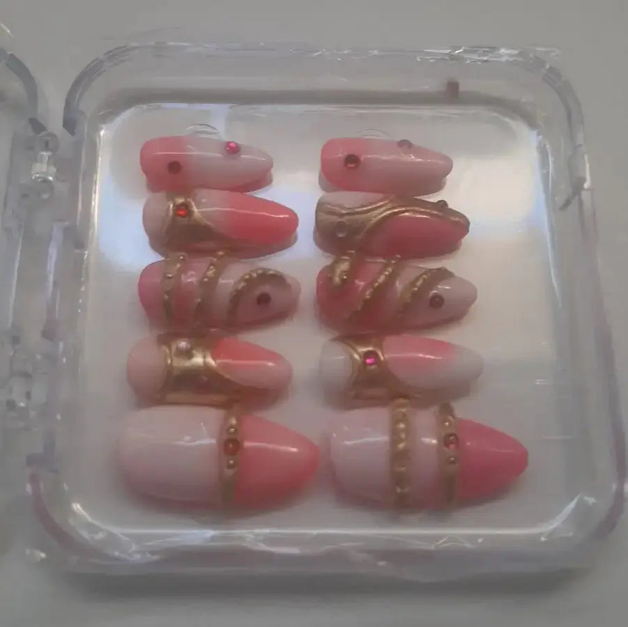 Vue sur le côté - Set de 10 press-on nails présentant des ongles dans des tons roses nude et corail, ornés de motifs serpentins dorés métallisés et de strass rouges.