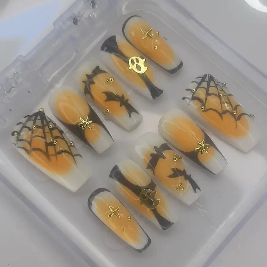 faux ongles sur une base blanche, aura orangé et designs halloween et décorations dorés