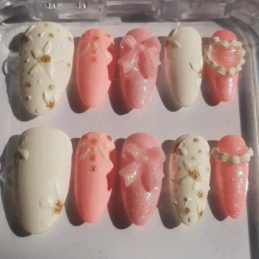 et de 10 faux ongles élégants dans des tons nude, rose poudré et transparent, ornés de strass dorés et décorations scintillantes, disposés sur fond blanc pour manucure professionnelle
