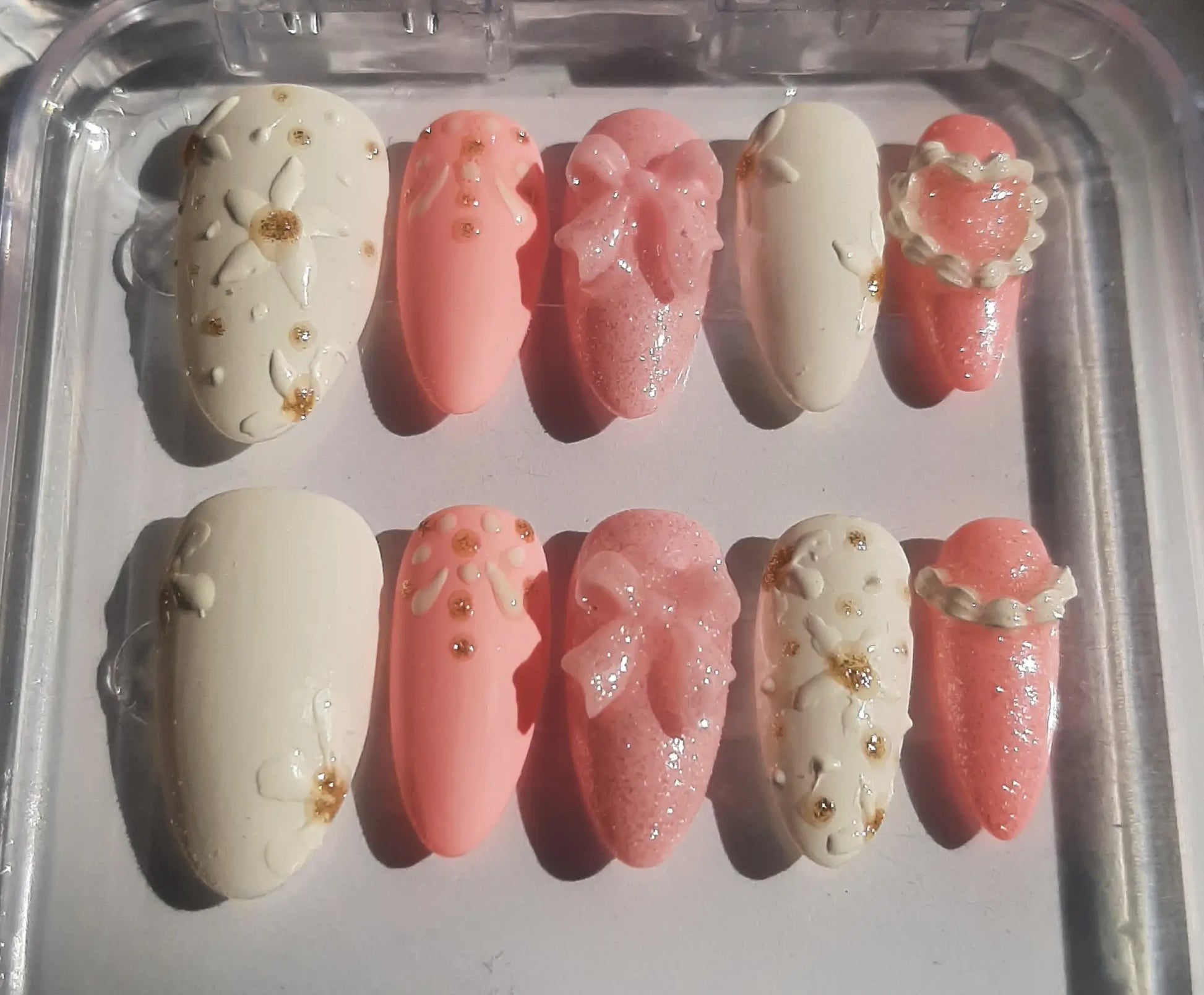 Set de 10 faux ongles élégants dans des tons nude, rose poudré et transparent, ornés de strass dorés et décorations scintillantes, disposés sur fond blanc pour manucure professionnelle
