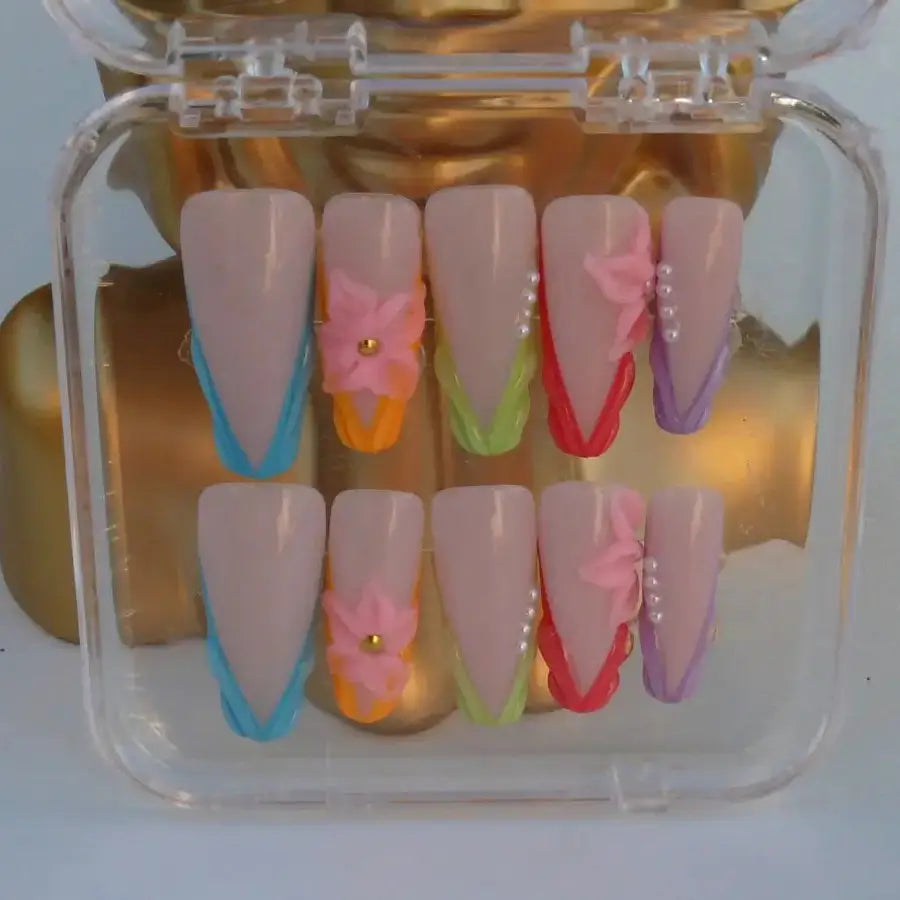 Vue détaillée des faux ongles Emy french triangle couleurs bleu orange vert violet sur une base nude et fleurs 