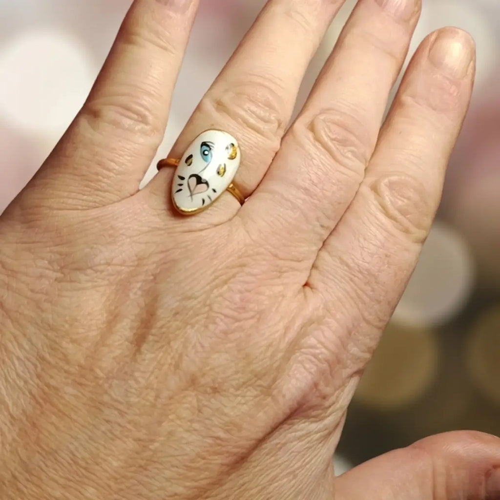 Bague ovale dorée avec médaillon tigre blanc aux yeux bleus et taches dorées peint à la main, portée à l'annulaire, bijou artisanal unique