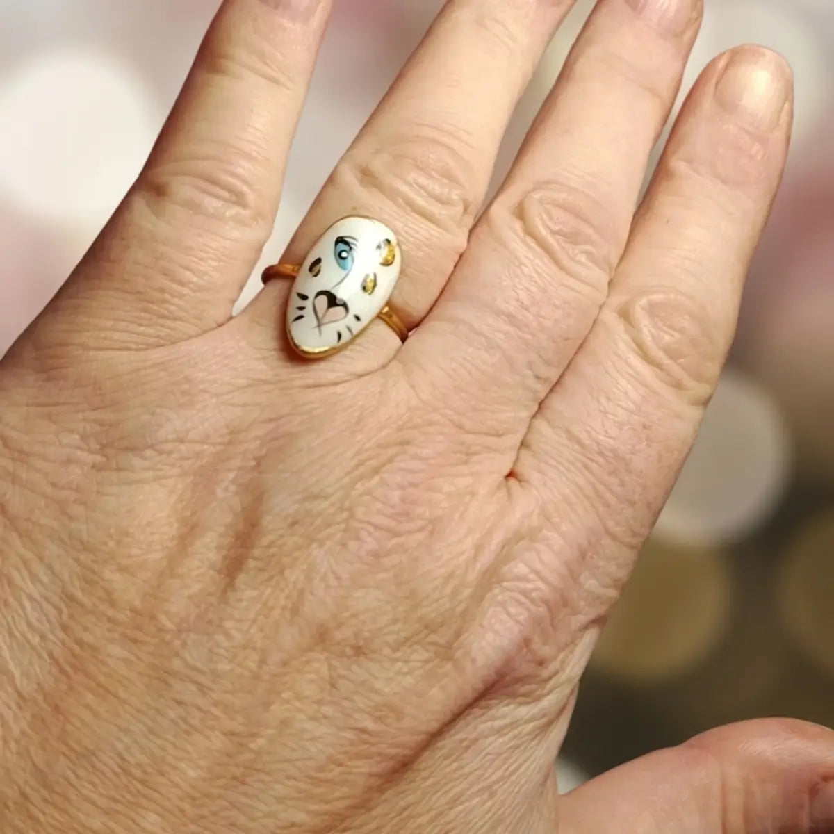 Bague ovale dorée avec médaillon tigre blanc aux yeux bleus et taches dorées peint à la main, portée à l'annulaire, bijou artisanal unique