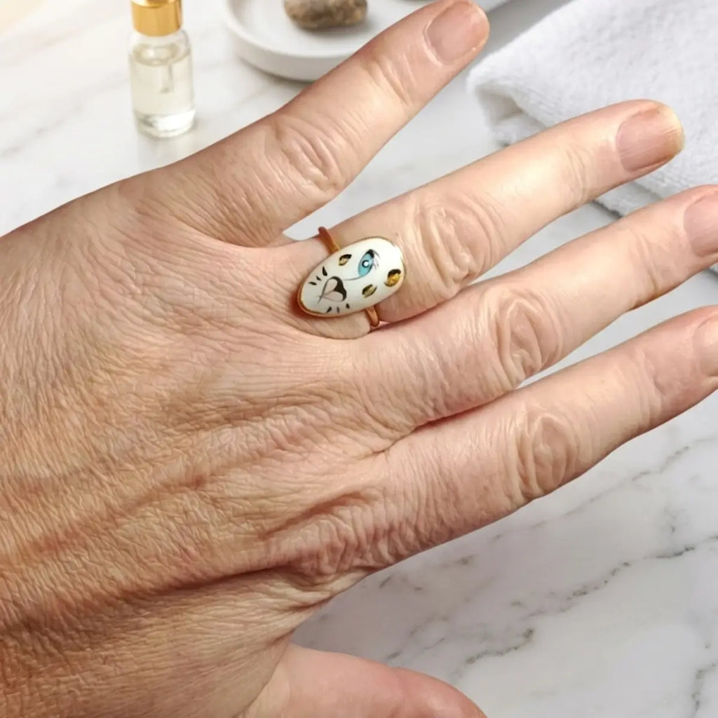 Bague ajustable en acier inoxydable doré avec ongle artisanal tigre blanc peint à la main, portée sur doigt, fond atelier nail art