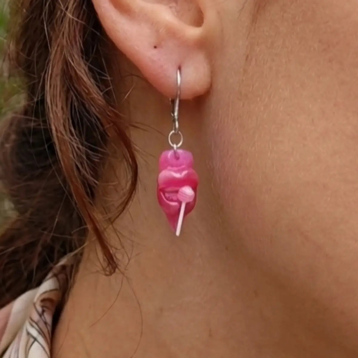 Boucle d'oreille argentée avec pendentif résine en forme de lèvres roses tenant une sucette, portée par une femme aux cheveux bruns — bijou Candy Lips Nail'Style