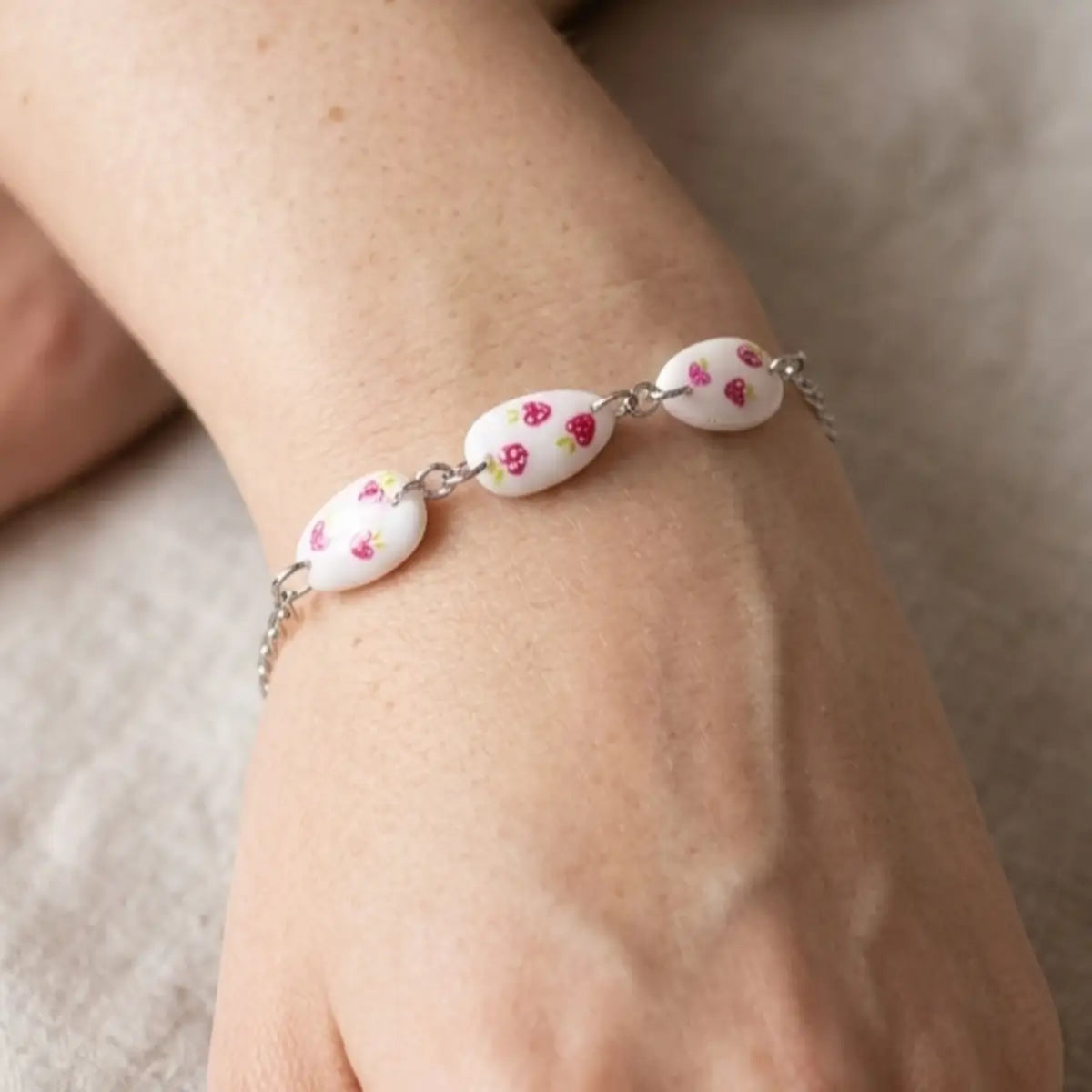 Bracelet chaîne argentée avec trois pendentifs en forme d'ongle amande, fond blanc motifs fraises roses — NailStyle