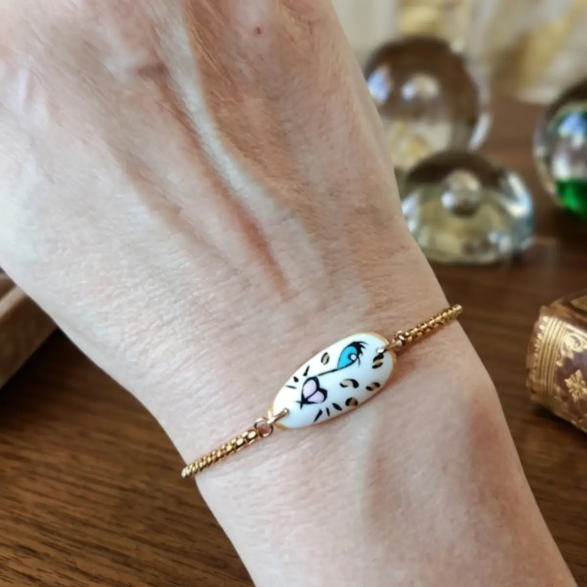 Bracelet chaîne dorée avec médaillon tigre blanc aux yeux bleus peint à la main, porté au poignet, accessoire artisanal unique