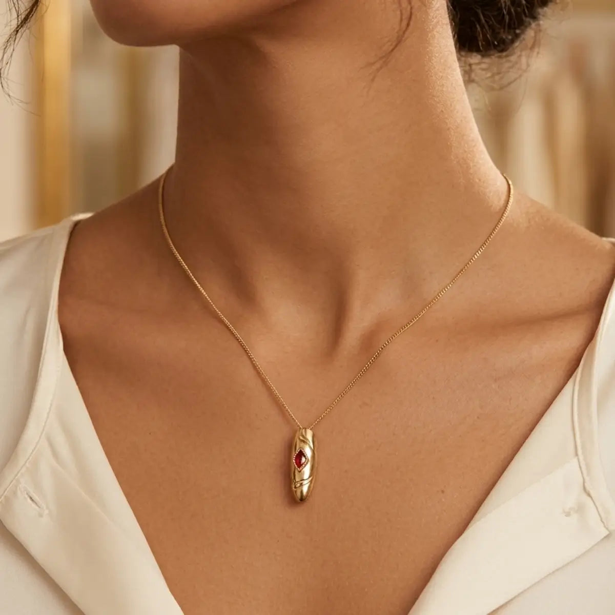 Collier pendentif ovale doré avec pierre rouge rubis, porté sur chaîne fine dorée, style élégant et minimaliste