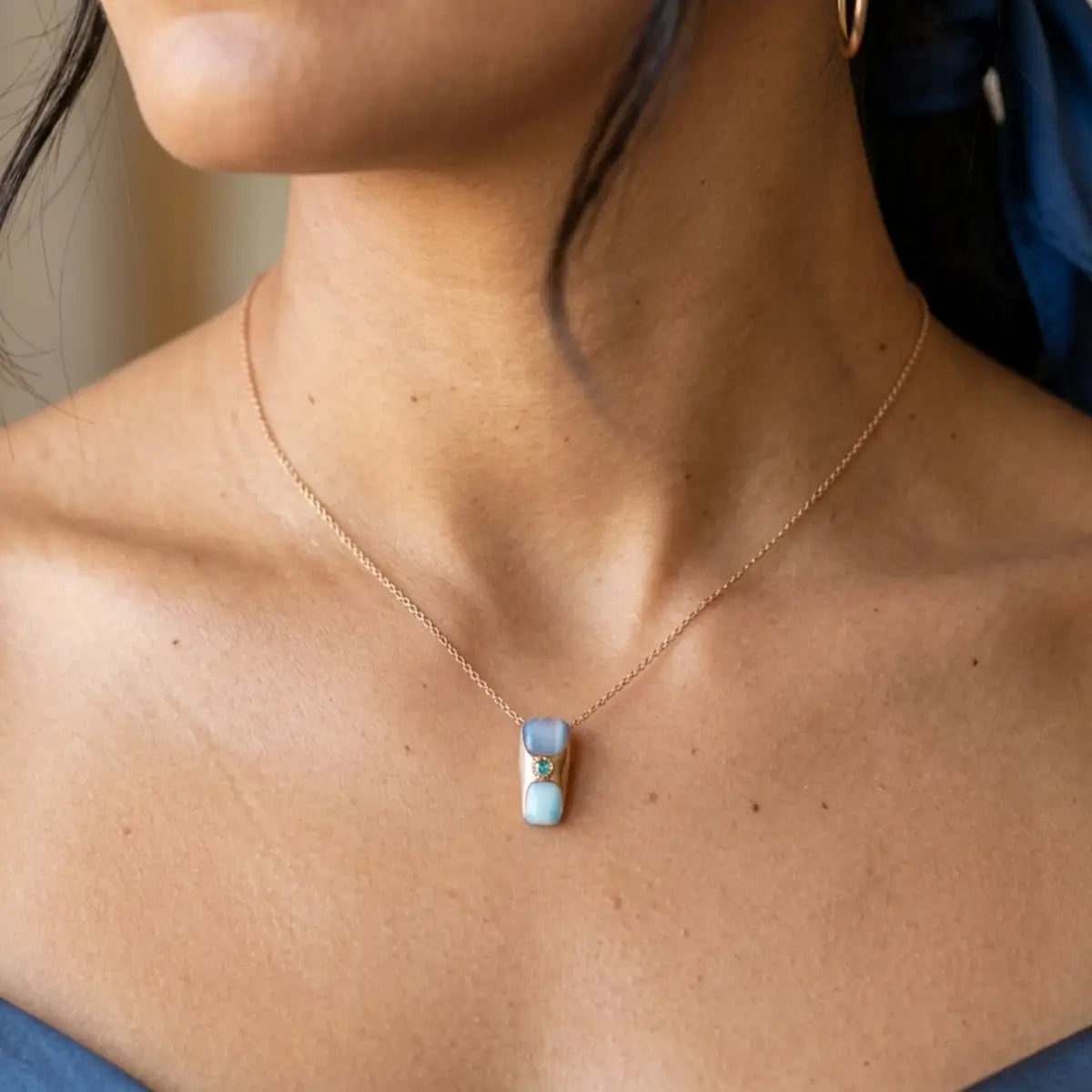 Collier pendentif double pierre bleue cat eye et chrome sur chaîne dorée rosé, porté sur décolleté féminin, ambiance lumineuse et élégante