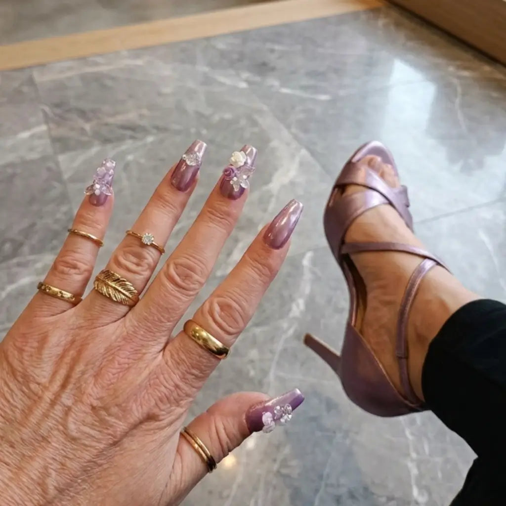 Faux ongles Florane violet irisé cat eyes effet 3D avec papillons transparents et perles, portés avec bagues dorées.