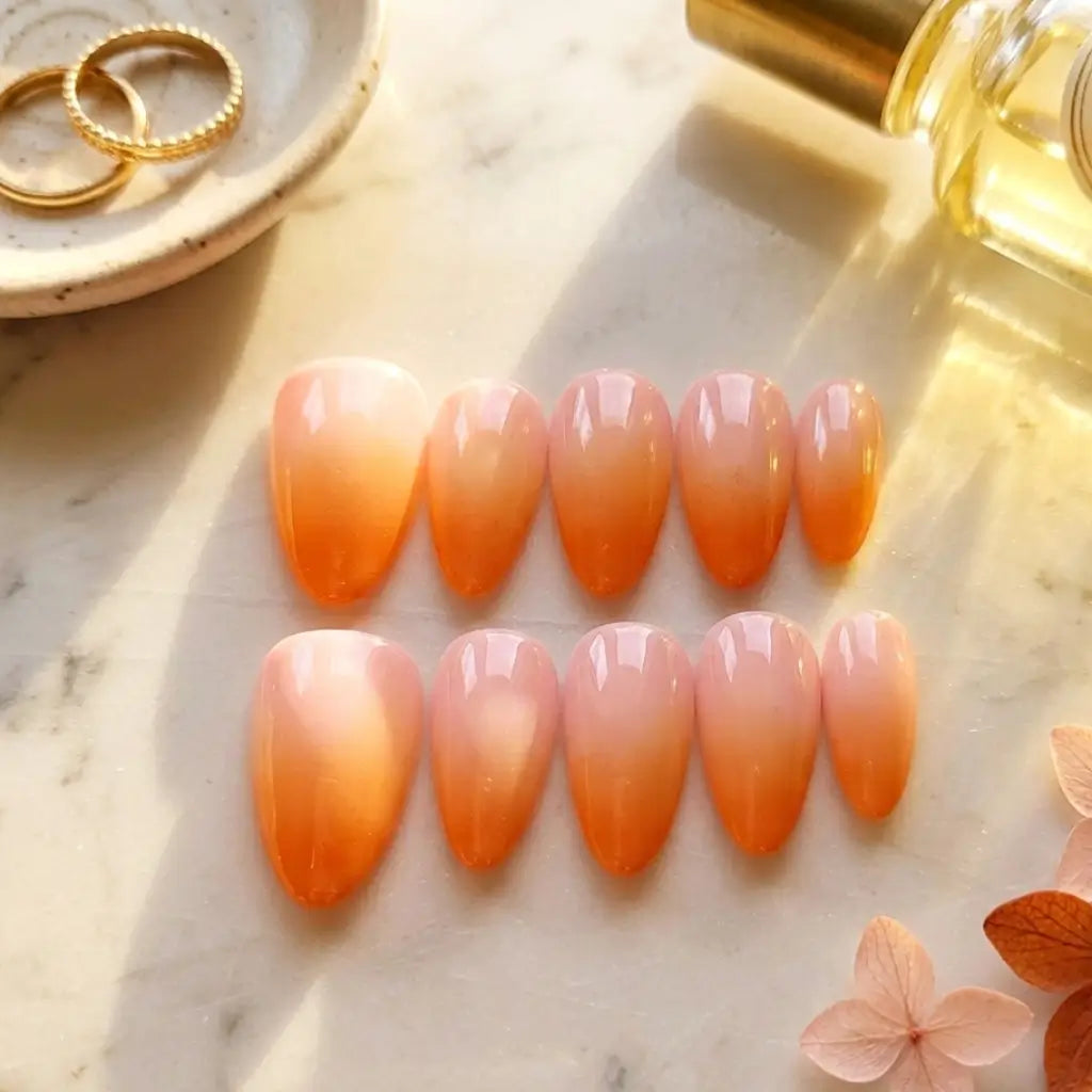 Faux ongles Peach Glow fabrication artisanale française, dégradé rose orange sur marbre blanc avec accessoires dorés.