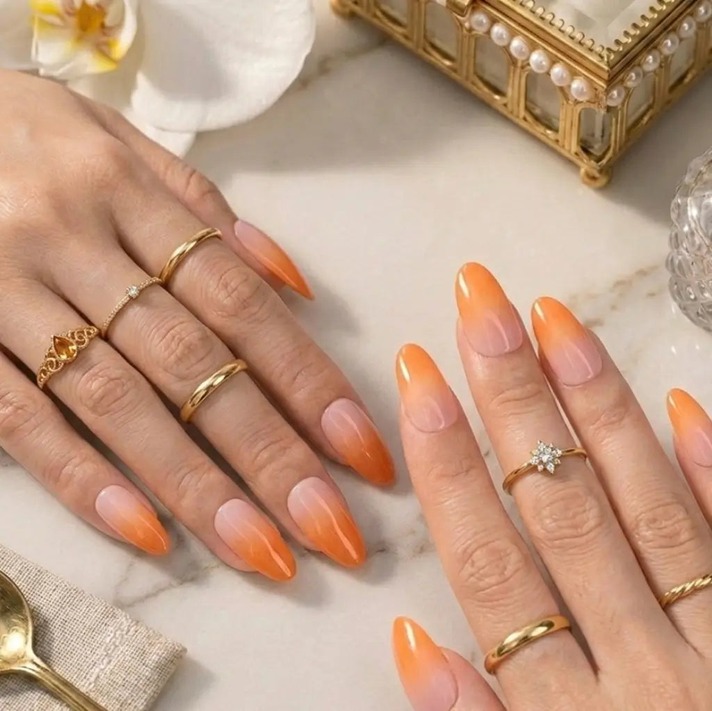 Faux ongles Peach Glow dégradé orange rose portés sur deux mains avec bagues dorées et bague solitaire diamant.