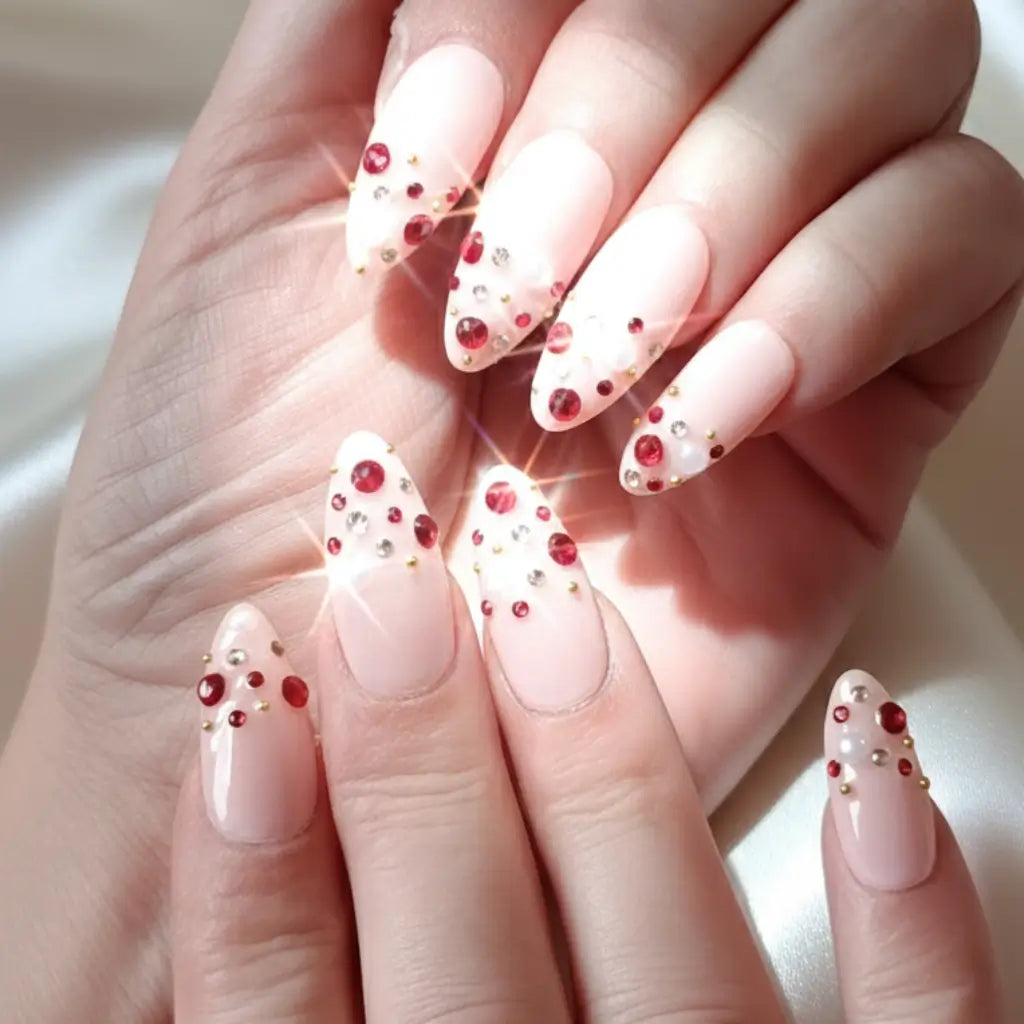 Faux ongles réutilisables rose nude avec strass rouges et dorés portés sur deux main