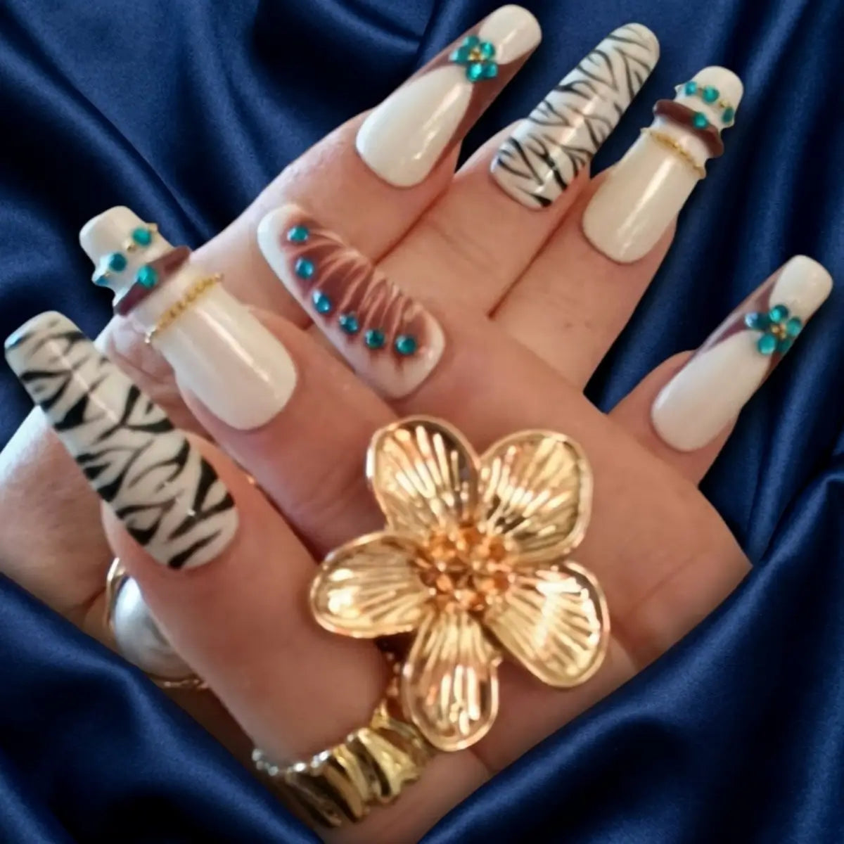 Faux ongles réutilisables blanc à motifs zèbre noirs et strass turquoise portés avec bagues dorées - NailStylefr