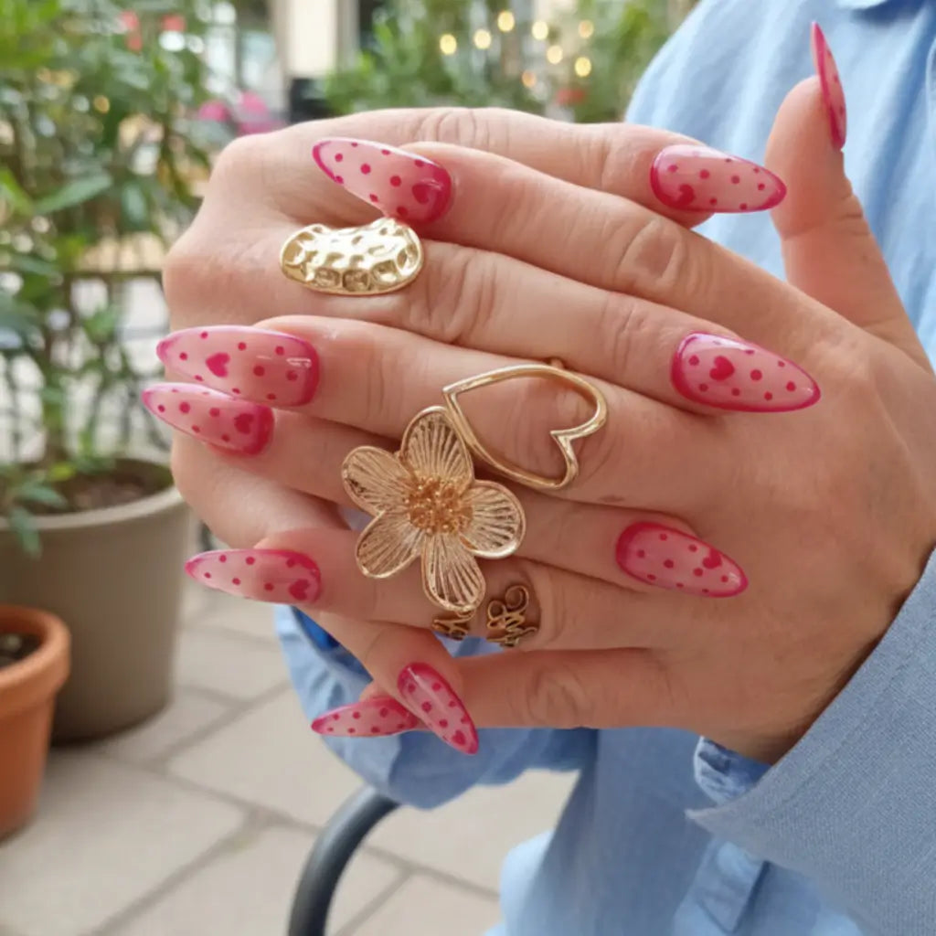 Faux ongles réutilisables rose fushia à cœurs et pois portés sur main avec bagues dorées fleurs et cœurs.