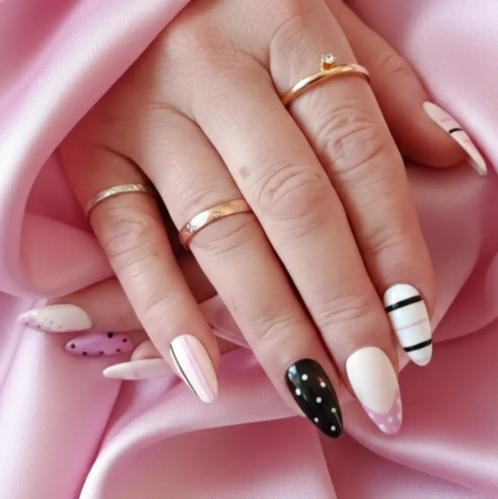 Faux ongles réutilisables portés sur main avec bagues dorées, motifs rose, blanc et noir à pois et rayures.  Fabrication Artisanale Française.
