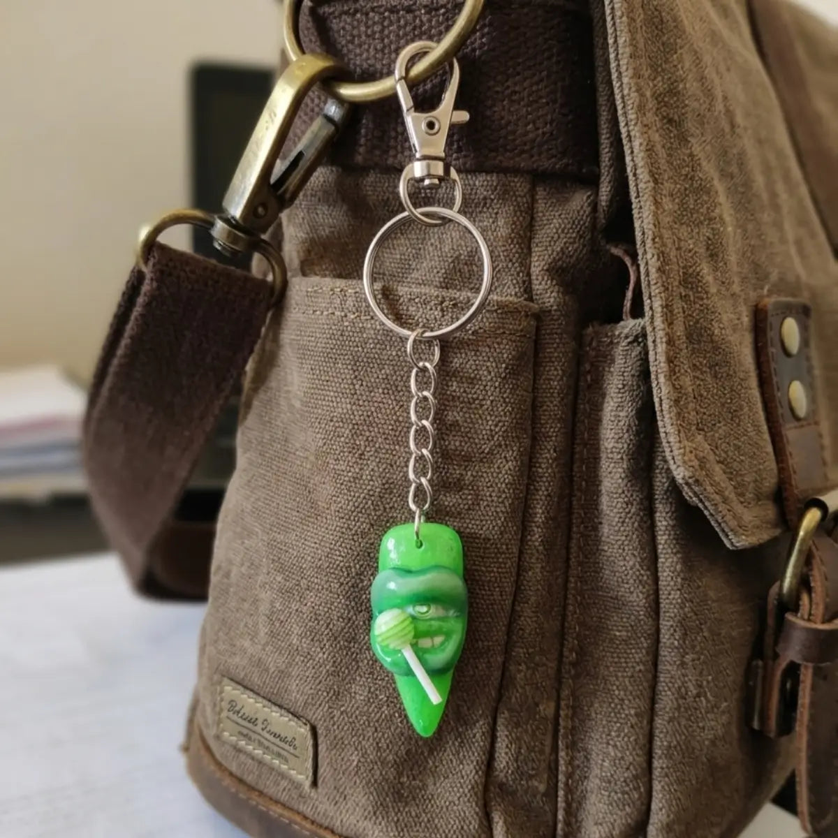 Porte-clés résine artisanal en forme de lèvres vertes tenant une sucette, accroché à un sac en toile marron — bijou de sac Shego Lips Nail'Style