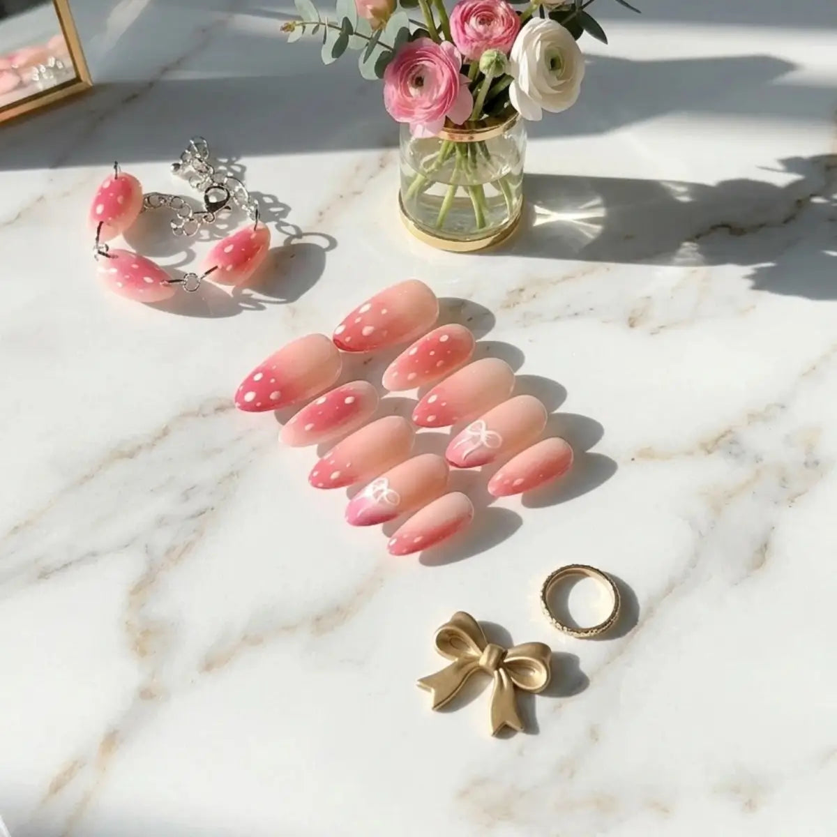 Gros plan sur set de faux ongles forme amande Bambi, dégradé rose corail avec pois blancs et nœud délicat, posés sur marbre blanc.