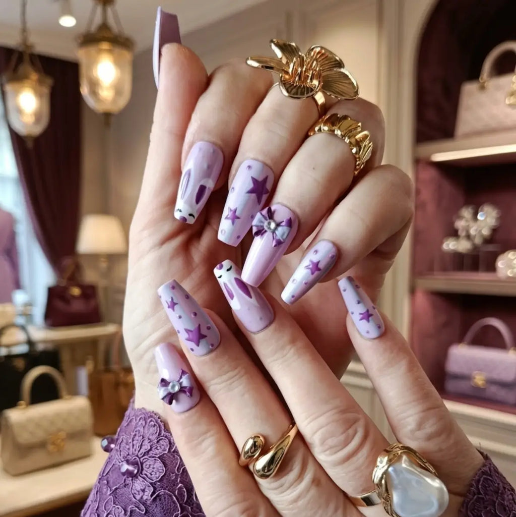 Set de press-on nails Bunny Vibes forme coffin – vue portée sur deux mains, coloris lilas et rose poudré avec étoiles et nœud 3D