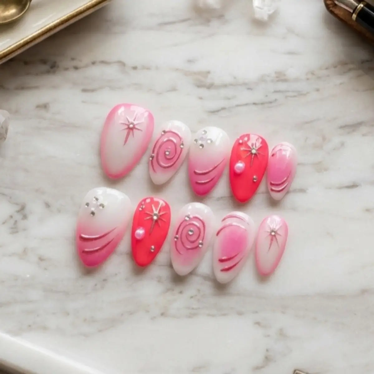 Kit press-on nails Candy Galaxie 10 ongles sur marbre blanc, dégradé blanc-rose-rouge avec motifs galaxie, strass et perles nacrées.