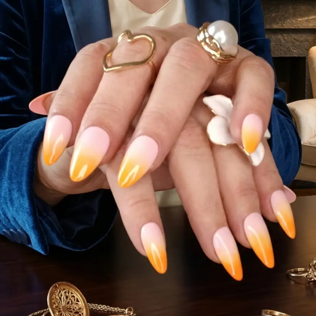 Press-on nails Peach Glow orange sur base rose portés avec bagues dorées cœur et perle, ambiance luxe.