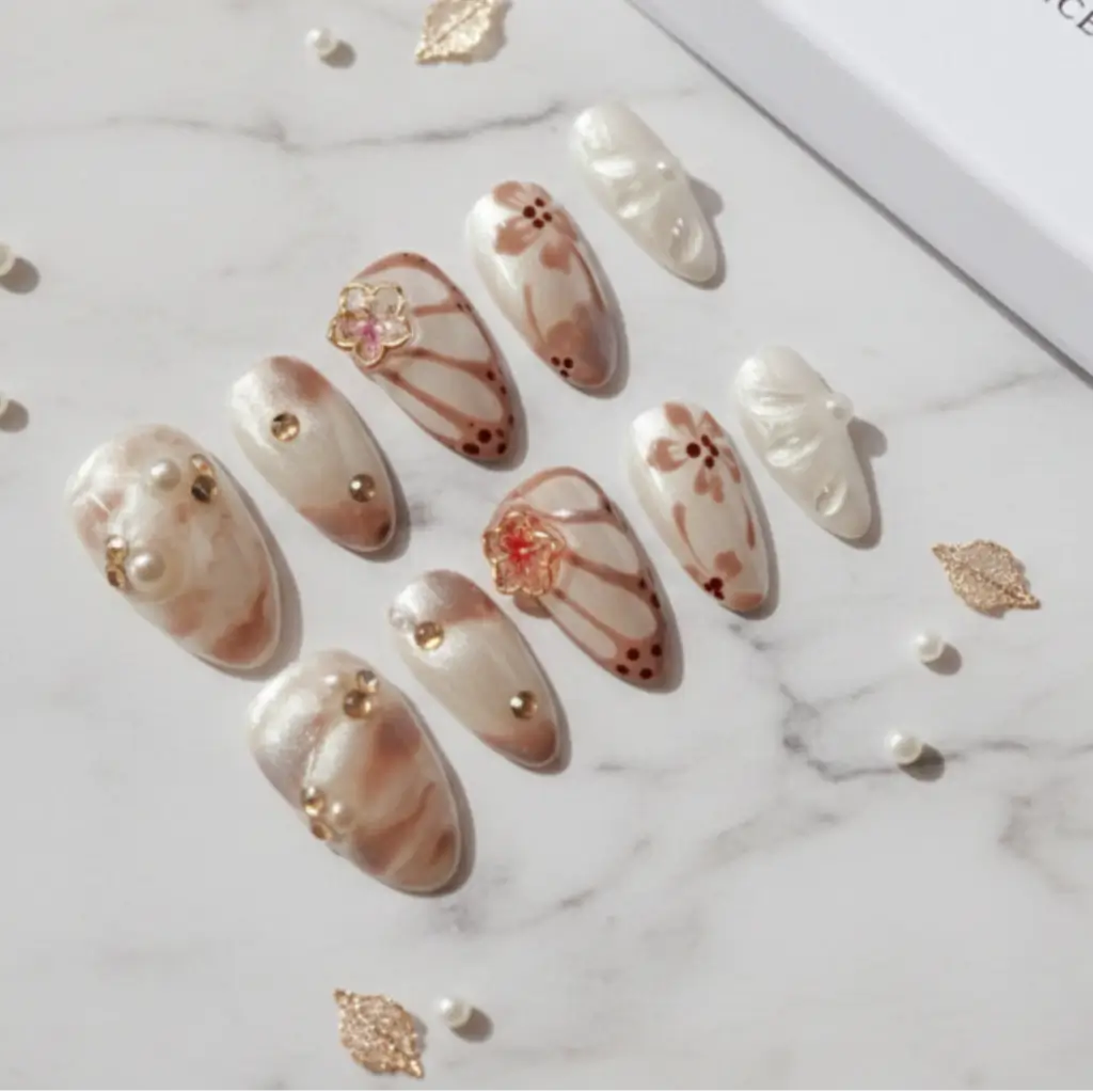 Faux ongles press-on ultra-tendance avec motifs floraux et strass. sublime. Nacre blanc pure et marron, fleurs 3 et strass. Forme Amande.