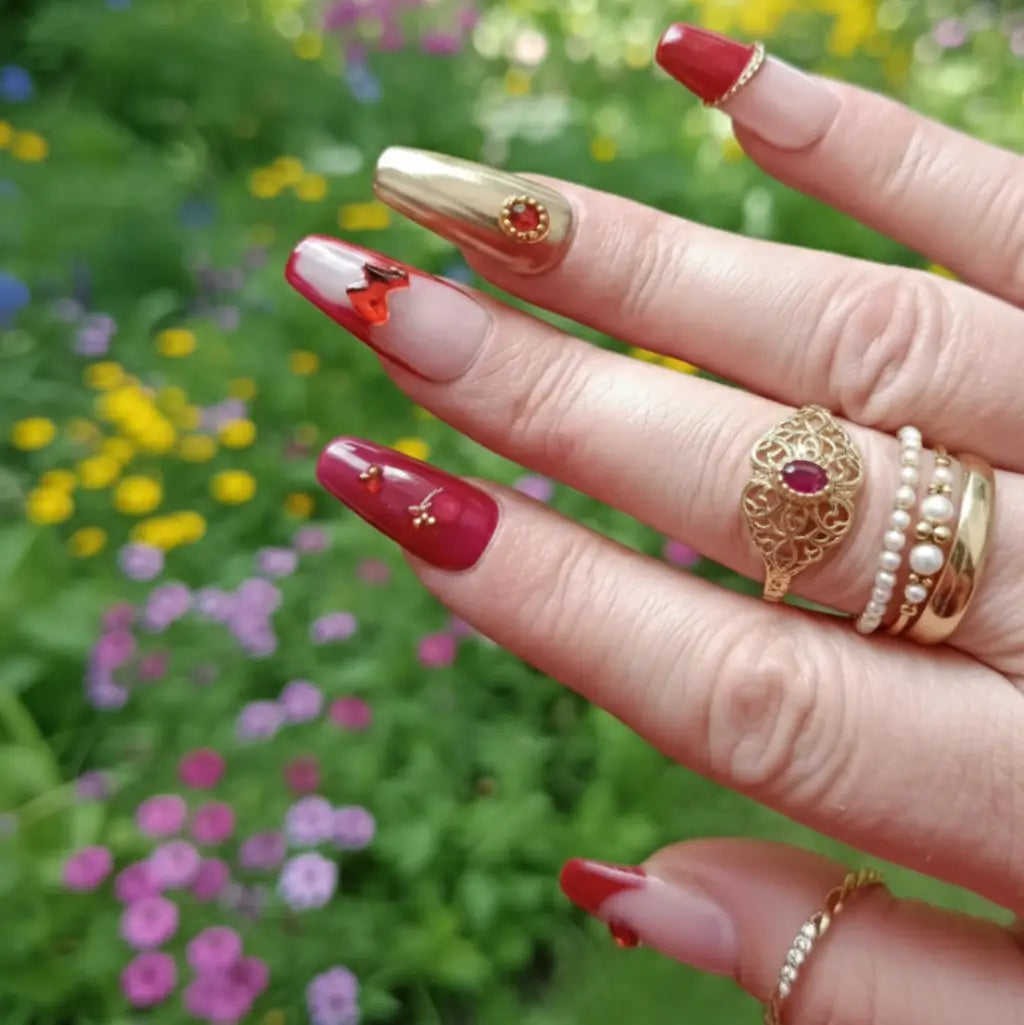 Faux ongles Royal Garnet rouge et nude portés, design élégant avec strass et détails dorés.