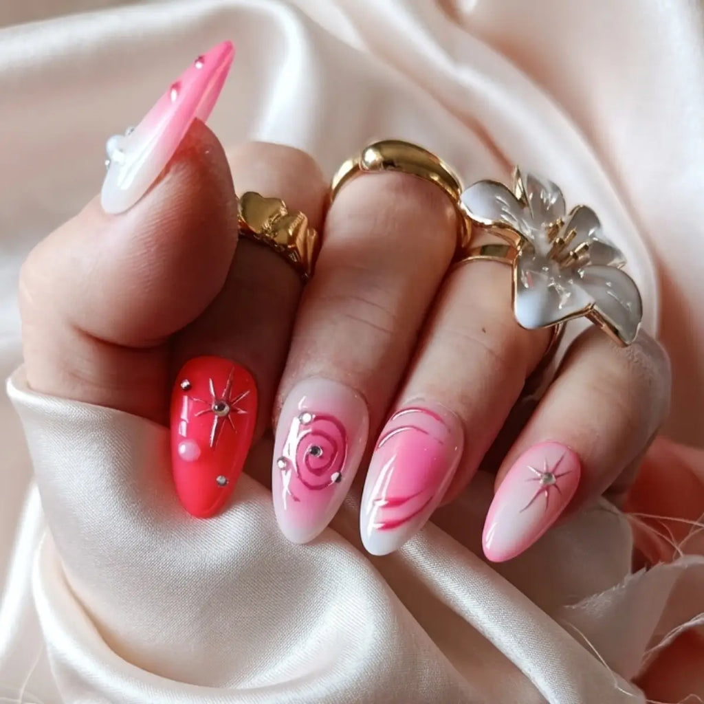 Press-on nails Candy Galaxie rose et rouge sur fond satin blanc, motifs spirale et étoile filante avec strass argentés, forme amande longue