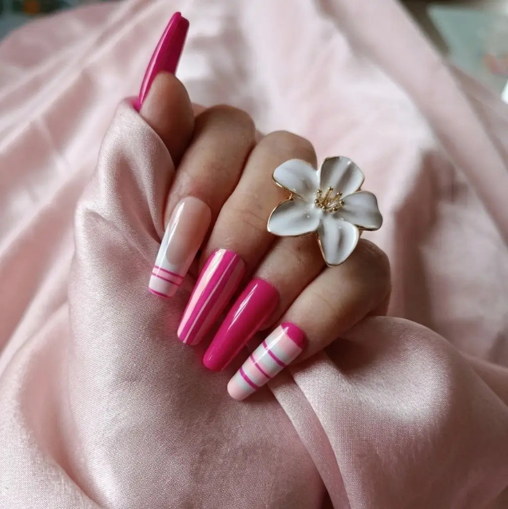 Press-on nails Candy Line rose fuchsia et blanc avec rayures minimalistes, forme coffin longue portés avec bague fleur blanche.