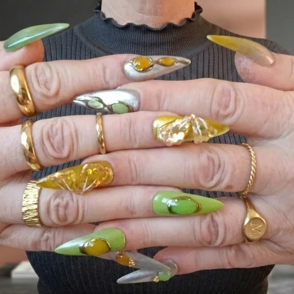 Press-on nails Jade Ambert portés - ongles stiletto verts et jaunes avec ornements dorés et effet chrome - manucure luxe réutilisable.