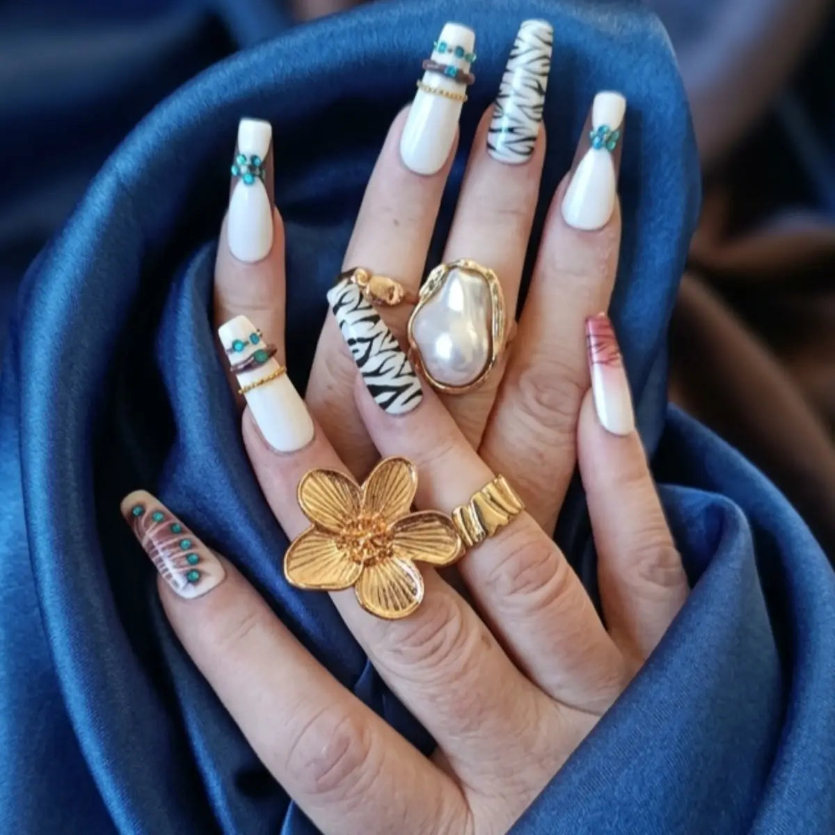 Faux ongles réutilisables blanc à motifs zèbre et strass turquoise portés avec bagues dorées - Nail'Style