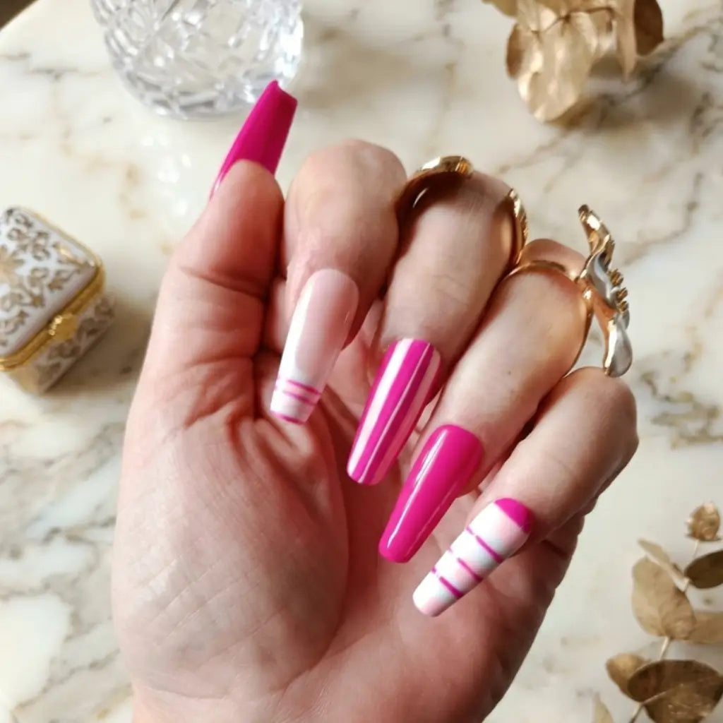 Press-on nails Candy Line forme coffin rose fuchsia et blanc avec rayures, portés sur main avec bague fleur.