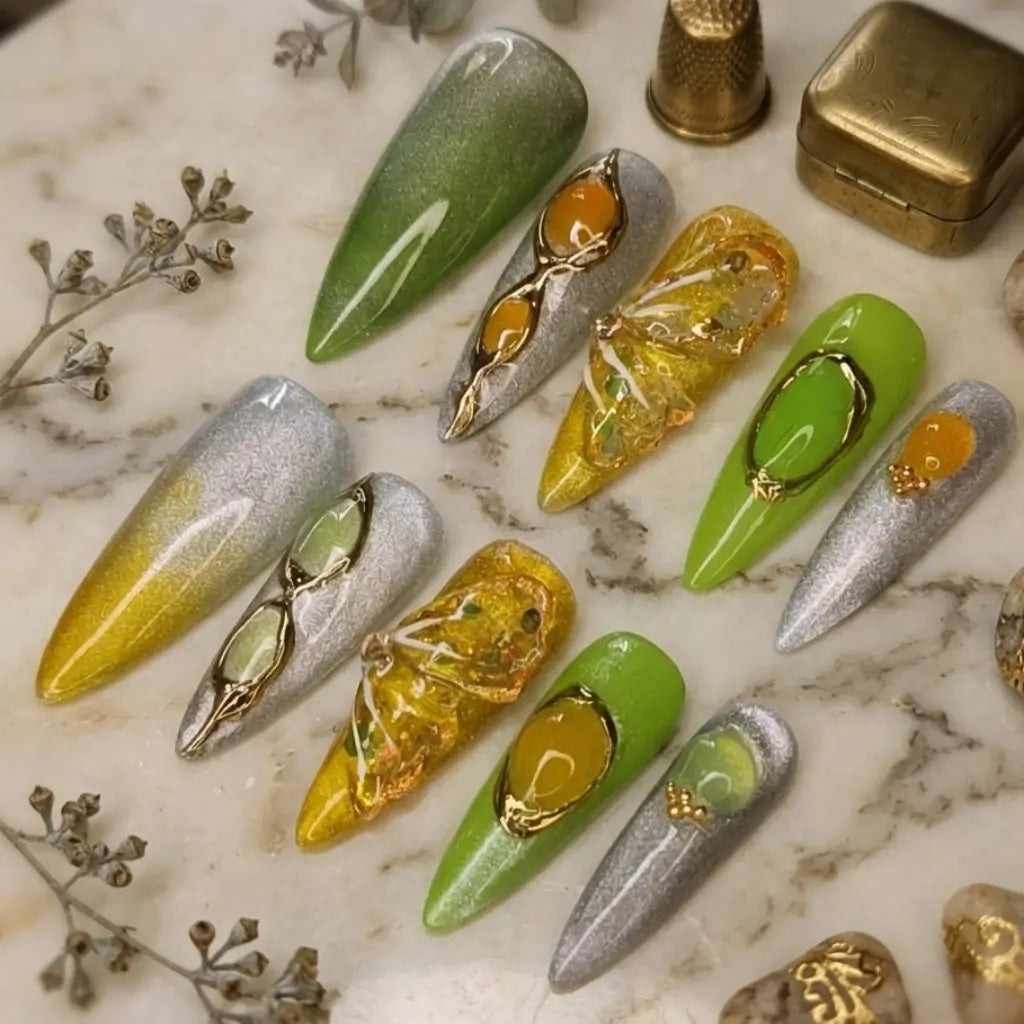 Faux ongles Jade Amber forme stiletto long avec dégradé vert olive, jaune doré et chrome argenté, bijoux 3D dorés.