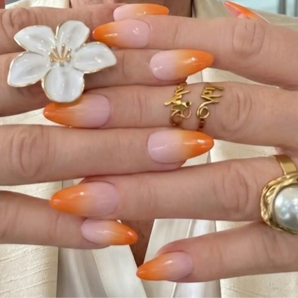 Faux ongles Peach Glow dégradé rose orange portés avec fleur blanche et bagues dorées, livraison rapide.