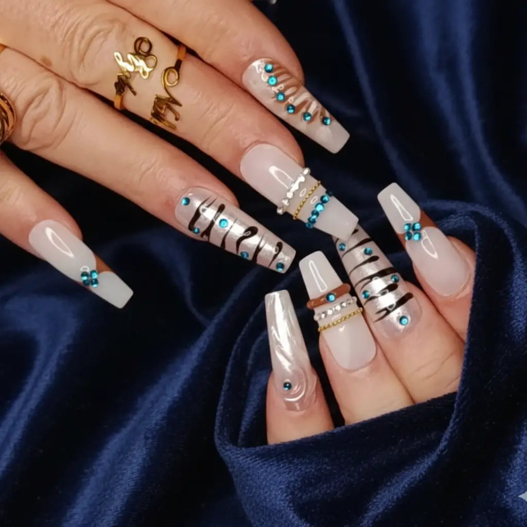 Faux ongles réutilisables blanc à motifs zèbre noirs et strass turquoise portés avec bagues dorées - Nail'Style