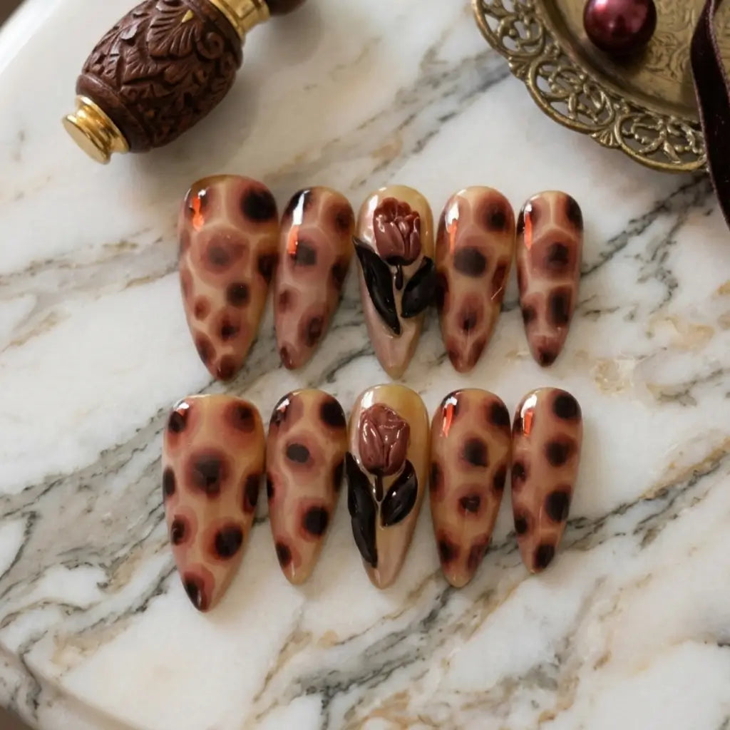 Gros plan sur les press-on nails Animals Garden posés sur une table marbrée. Marron et noir.