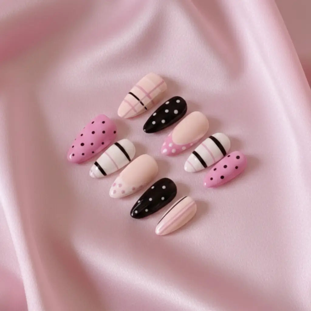 Gros plan sur faux ongles réutilisables rose, blanc et noir à pois et rayures disposés sur tissu rose