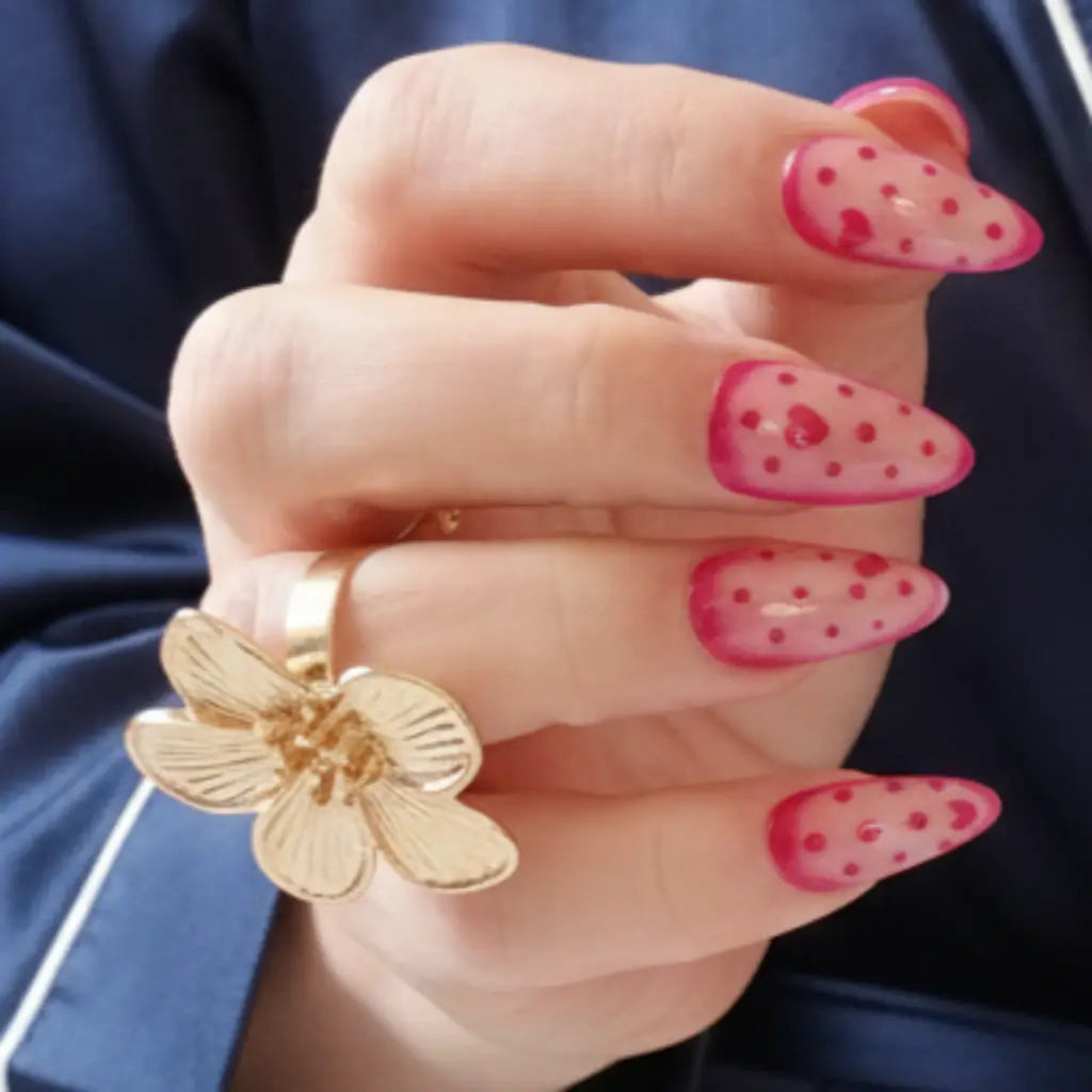 Vue latérale faux ongles réutilisables rose à cœurs et Polka Dots portés avec bague dorée fleur.