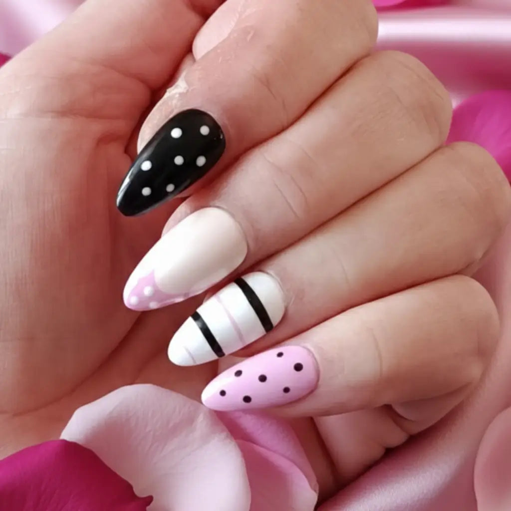 Faux ongles réutilisables portés sur main avec motifs à pois noir et rose, rayures noires sur fond blanc nacré
