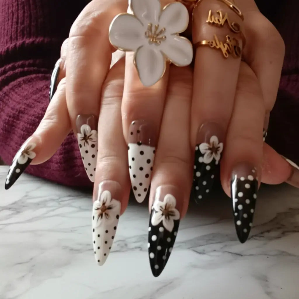 Faux ongles réutilisables noir et blanc portés avec bagues dorées - design floral élégant - Nail'Style